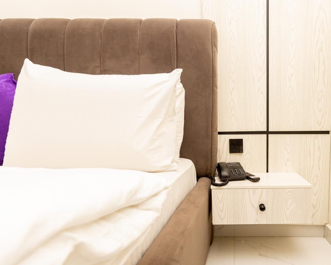 A hotel room with a bed, a nightstand with a telephone, and a wooden wardrobe.