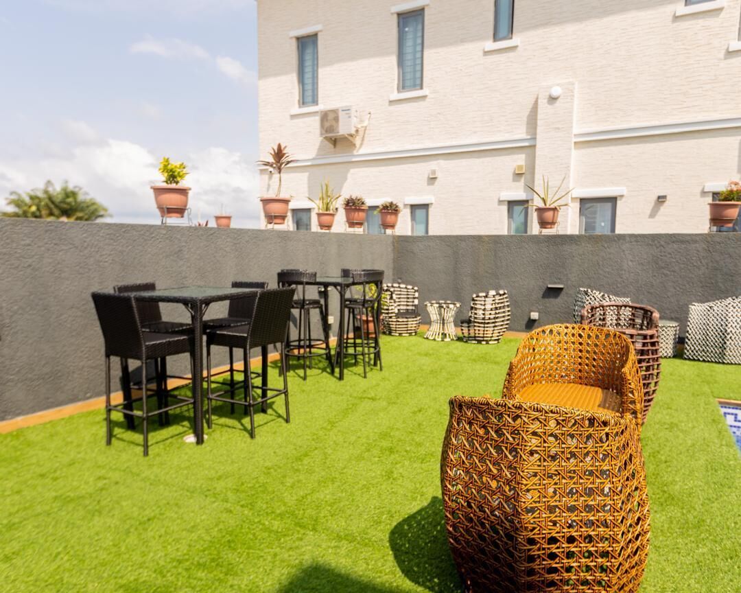 An outdoor patio with a green lawn, black metal chairs, wicker sofas, and potted plants.