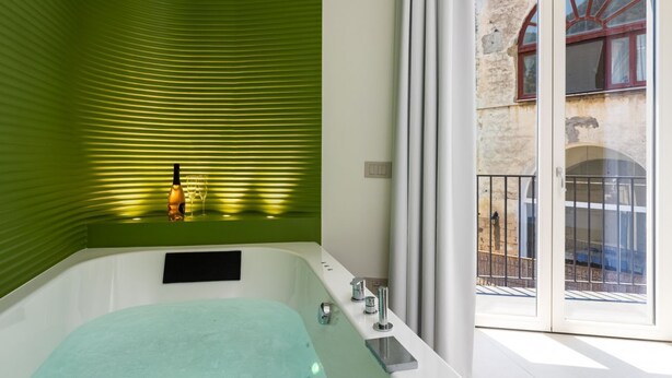 A modern bathroom with a green wall, a bathtub, and a balcony with a view of a building.