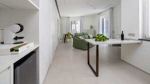 A modern kitchen with a built-in dishwasher, a dining area with a green sofa, and a small table with a plant.