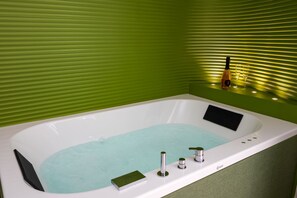 A modern bathroom with a bathtub, green walls, and a bottle of champagne. - Blue Sky Luxury Palace | Apartment with Private Jacuzzi near the Beach (Meta)