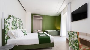 A hotel room with a bed, a chair, a TV, a bathroom, and a green accent wall.