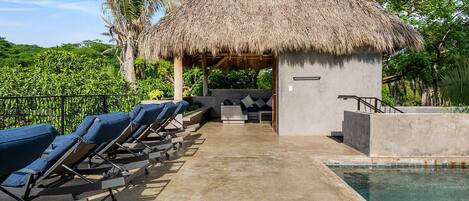 A poolside area with lounge chairs, a thatched-roof structure, and a pool.