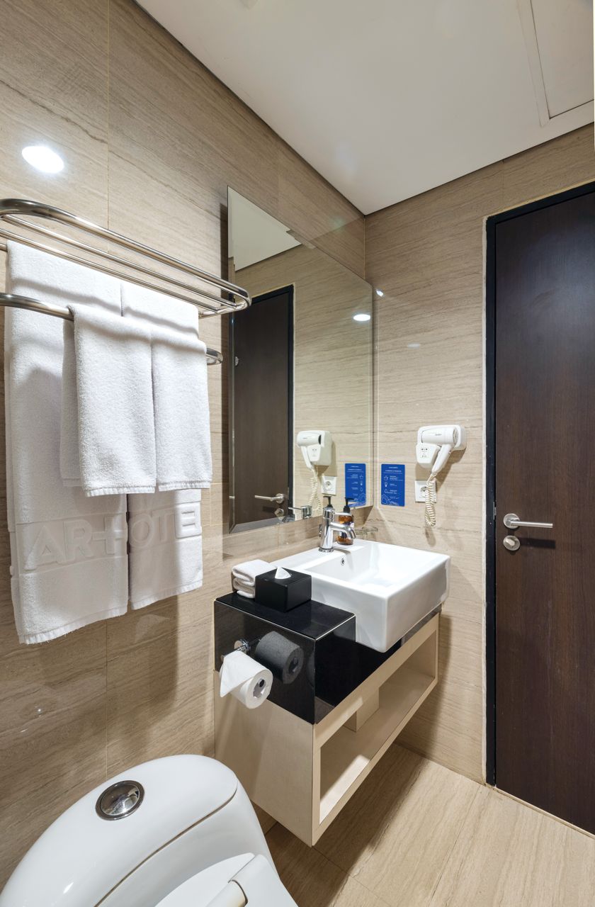 A modern bathroom with a white sink, a mirror, a towel rack with white towels, a toilet, and a hairdryer on the wall.