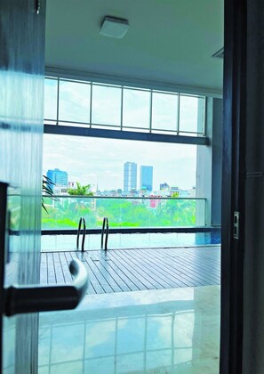 A room with a large window, a wooden deck, and a view of a cityscape. - Fairview Hotel by ARTOTEL (Jakarta)
