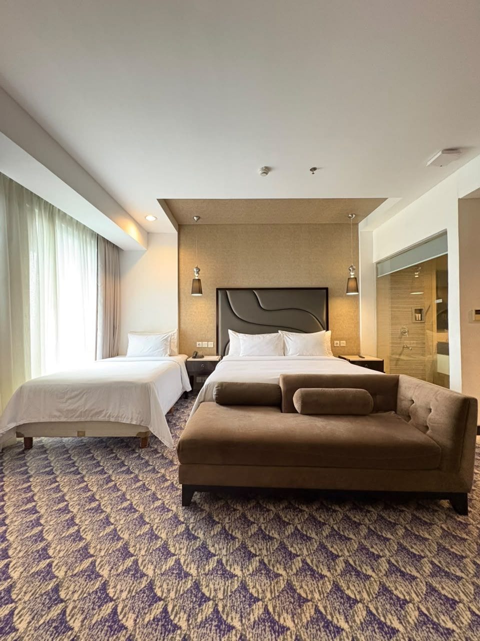 A hotel room with a large bed, a sofa, a desk, and a shower area.