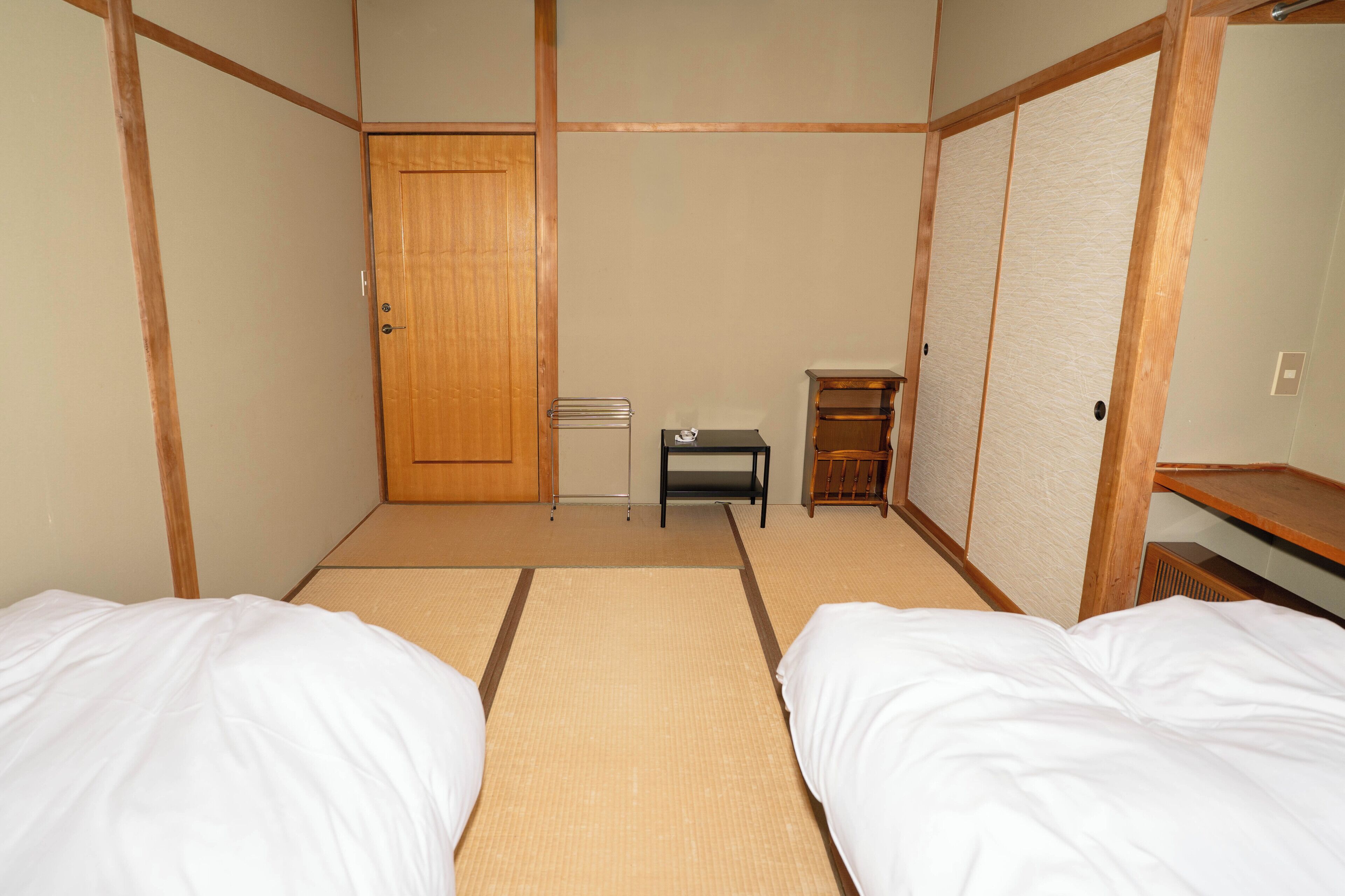 A room with two beds, a wooden door, a small table, and a shelf.