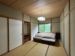 Una habitación tradicional japonesa con suelo de tatami, una cama baja, un armario de madera y una puerta corredera.