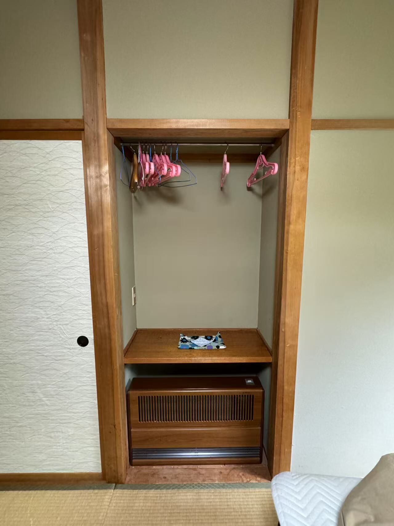 A wooden closet with a shelf, hanging clothes, and a small table.