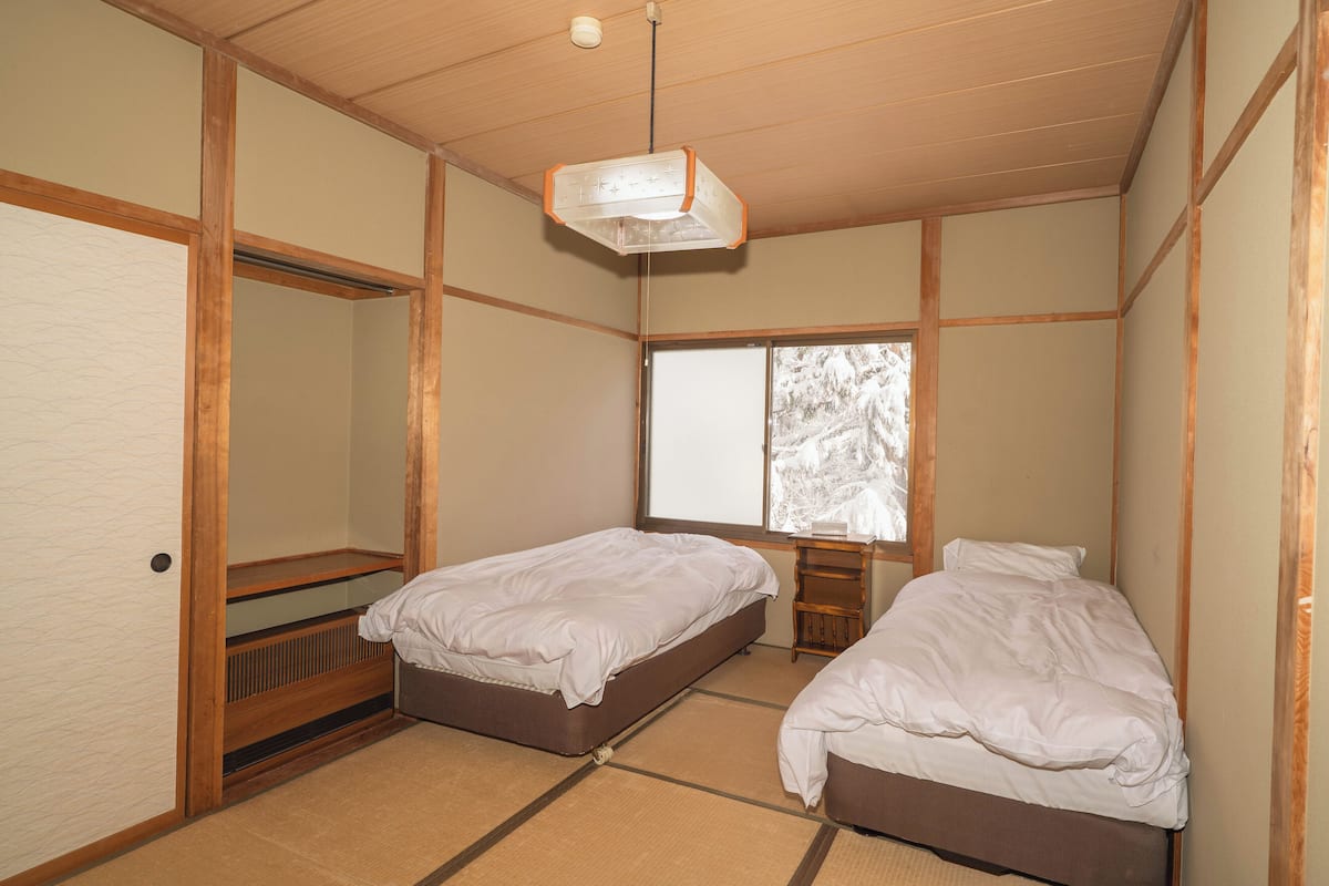 Een traditionele Japanse kamer met tatami vloeren, twee enkele bedden, een schuifdeur en een raam met uitzicht op besneeuwde bomen.