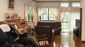 A living room with a fireplace, leather sofas, a television, and a large window with curtains. - Hotel Davos Hakuba (Hakuba)