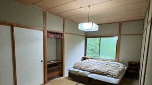 A traditional Japanese-style bedroom with tatami flooring, a bed, a hanging light fixture, and sliding doors. - Hotel Davos Hakuba (Hakuba)