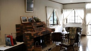 A living room with a brick fireplace, a dining table with chairs, and large windows with curtains. - Hotel Davos Hakuba (Hakuba)