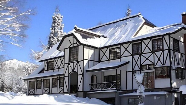 A traditional chalet-style building with a symmetrical facade, multiple windows, and a snow-covered roof, surrounded by a snowy landscape. - Hotel Davos Hakuba (Hakuba)