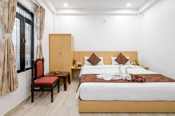 Una habitación de hotel con cama, escritorio, silla, armario y ventana con cortinas.