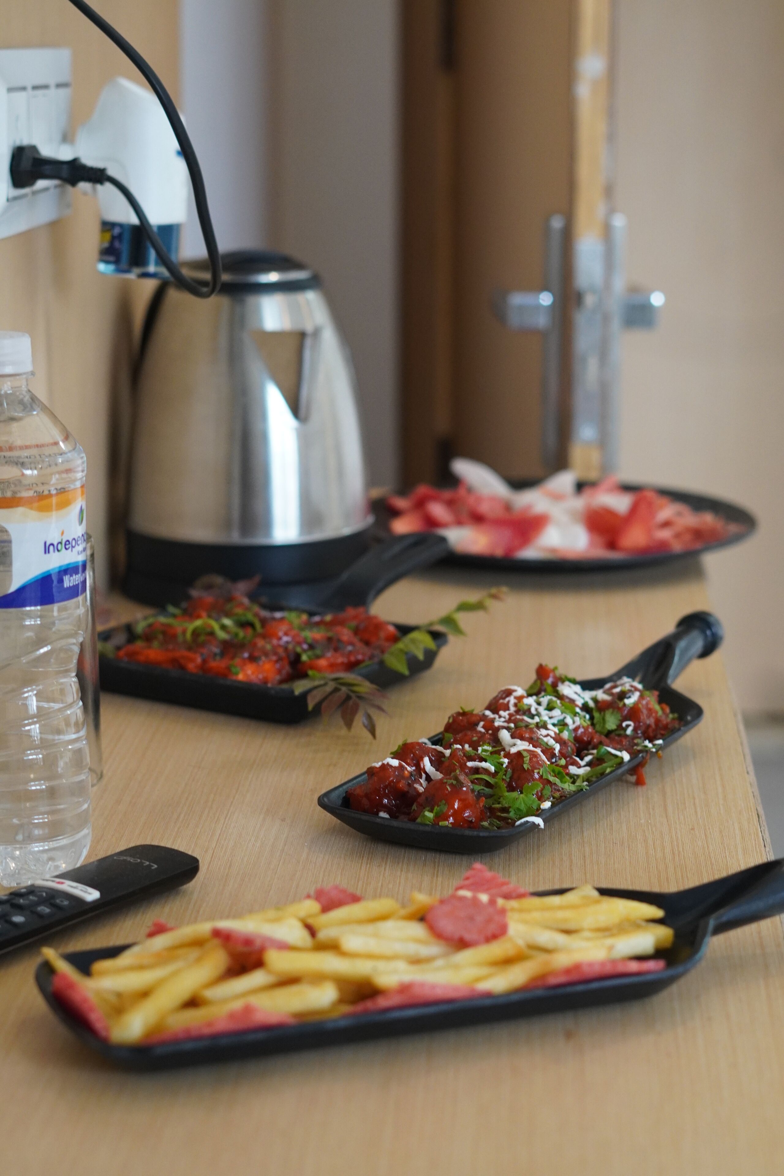 Una mesa con alimentos, una botella de agua, un hervidor y un control remoto.