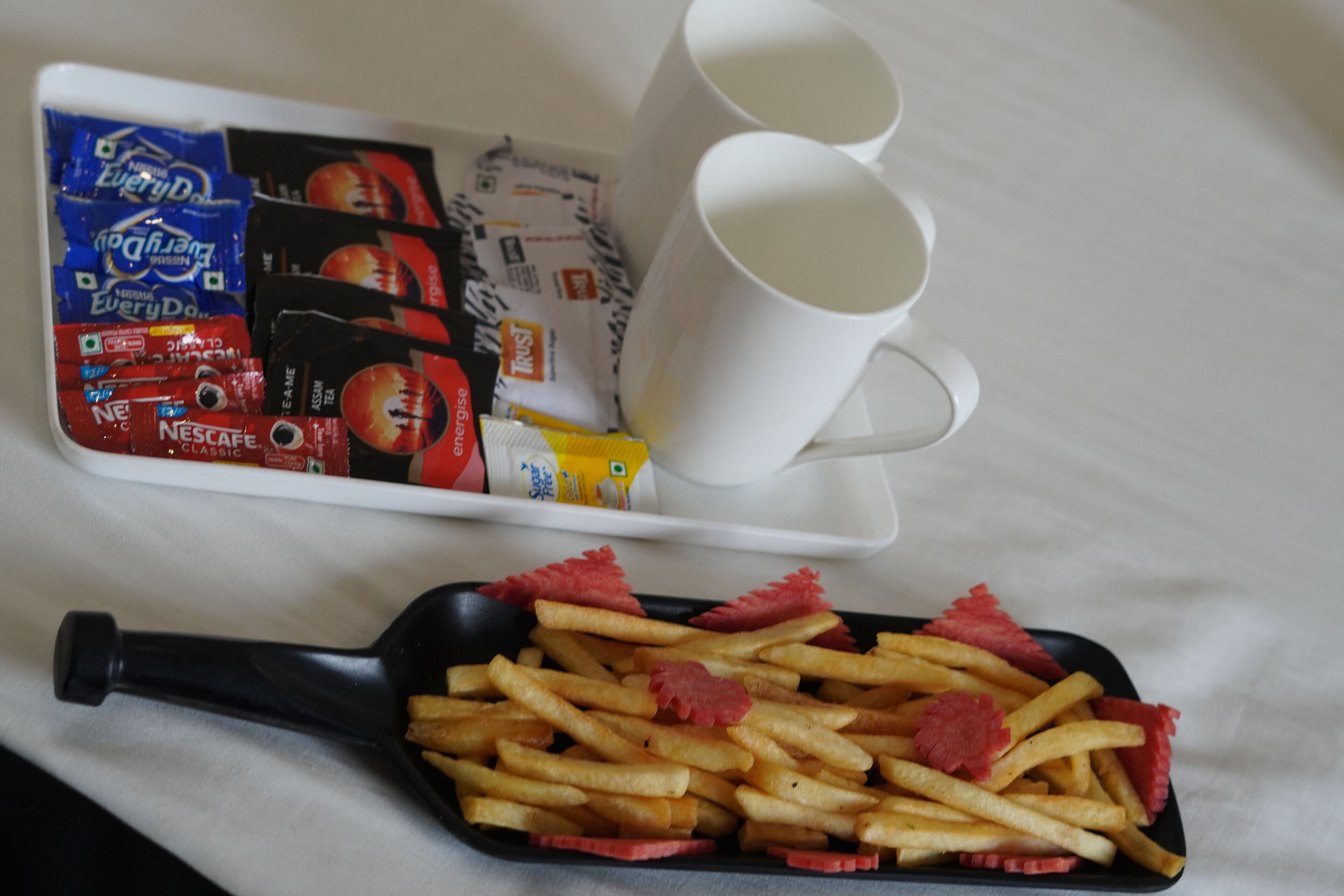 Una bandeja con papas fritas, dos tazas blancas y un paquete de café Nescafé Classic.