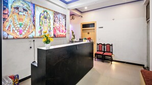 A reception area with a black marble counter, a chair, and two large religious paintings on the wall. - Hotel Kanak Kuteer (Ayodhya)