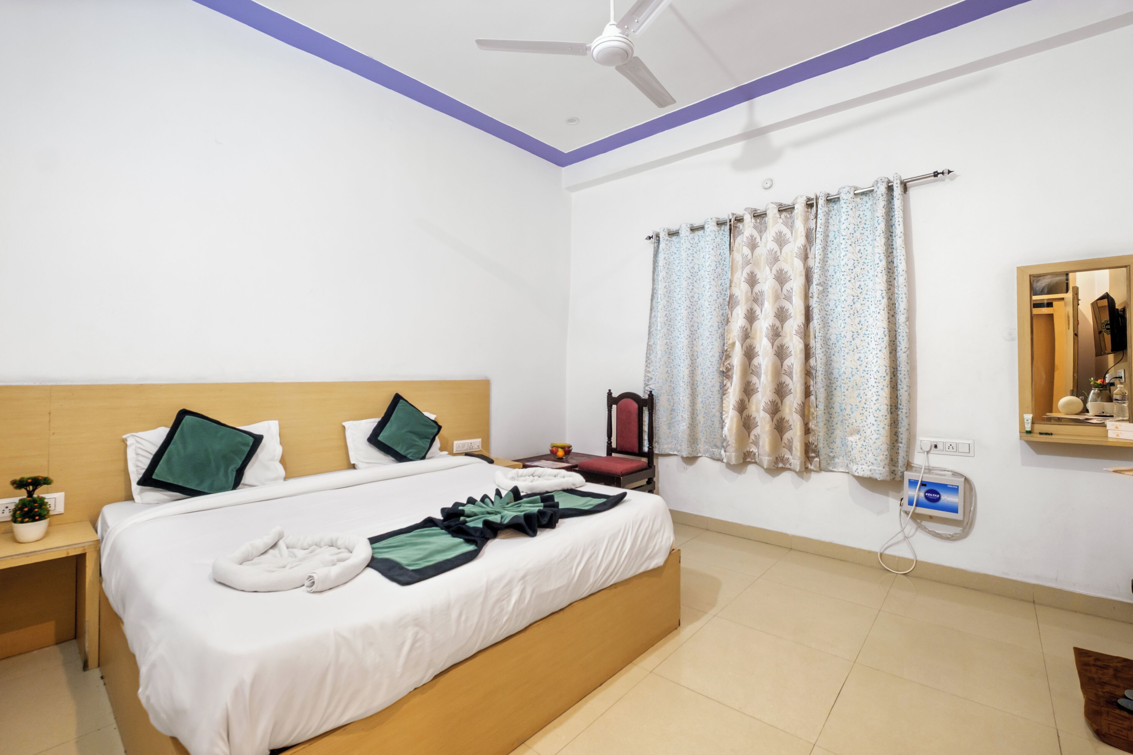 Une chambre d’hôtel avec un lit, une table de chevet, un miroir et un ventilateur de plafond.