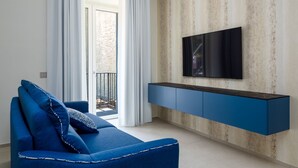 A modern living room with a blue sofa, a flat-screen TV mounted on a textured wall, and a balcony with white curtains.