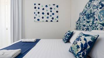Una camera d'albergo con un letto, cuscini, una testiera a motivi blu e bianchi, un quadro e una finestra con tende.