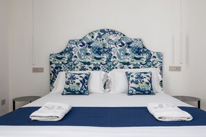 Ein Bett mit gemustertem Kopfteil, zwei Kissen und zwei gefaltete Handtücher auf einer blauen Bettdecke.