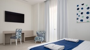 A hotel room with a bed, two chairs, a desk, a flat-screen TV, and a window with curtains.