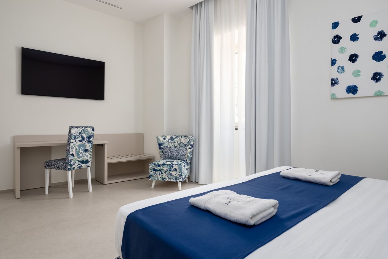 Una camera d'albergo con un letto, due poltrone, una scrivania, una TV a schermo piatto e una finestra con tende.