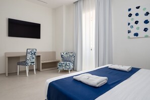 Una camera d'albergo con un letto, due poltrone, una scrivania, una TV a schermo piatto e una finestra con tende.