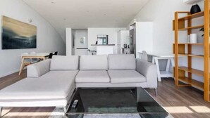 A modern living room with a sectional sofa, a glass coffee table, and a wooden bookshelf. - Spacious Penthouse With Spectacular Harbour Views! (Auckland)