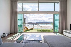 A modern living room with a glass coffee table, grey sofas, and a view of a balcony with outdoor furniture. - Princes Wharf Penthouse with Harbour Views (Auckland)