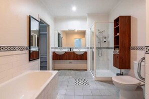 Une salle de bain moderne équipée d’une baignoire, de deux lavabos, d’une douche et de toilettes.