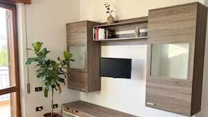 A modern living room with a large entertainment unit, a flat-screen TV, and a potted plant. - Alta Marea Portoscuso (SU) - 6 Beds, Seafront and Pinewood! (Portoscuso)