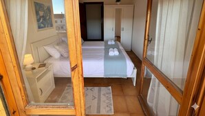 A bedroom with a bed, bedside table, lamp, and a view through a wooden-framed window. - Alta Marea Portoscuso (SU) - 6 Beds, Seafront and Pinewood! (Portoscuso)