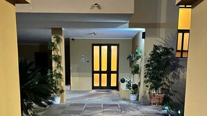 A building entrance with a tiled walkway, a glass door with vertical panels, and potted plants on either side. - Alta Marea Portoscuso (SU) - 6 Beds, Seafront and Pinewood! (Portoscuso)