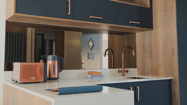 A modern kitchen with a Bosch toaster, a coffee maker, and a sink with a copper faucet.