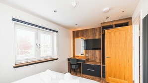 A bedroom with a bed, a desk, a chair, a wardrobe, and a window with blinds.