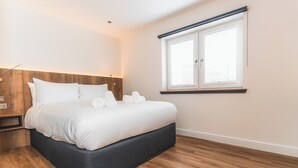 A modern bedroom with a large bed, wooden headboard, and a window with blinds.