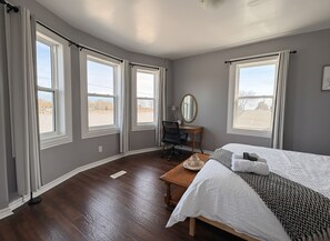 A bedroom with a bed, a desk, a chair, a mirror, and large windows. - Waterfront Cottage, Top Fishing Spot, Light House, Pet-Friendly (Dunville)
