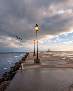 A coastal walkway with street lamps, a plaque, and a lighthouse in the distance.