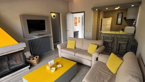 A modern living room with a sofa set, a yellow coffee table, a flat-screen TV, and a kitchen area with a refrigerator and microwave. - The Cozy Inn - Agate (Faqra - Kfardebiane,)