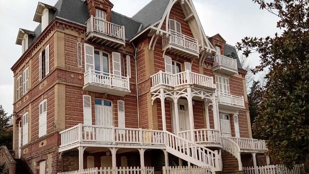 Un grand immeuble à plusieurs étages, doté d’un balcon imposant et d’un escalier menant à l’entrée.