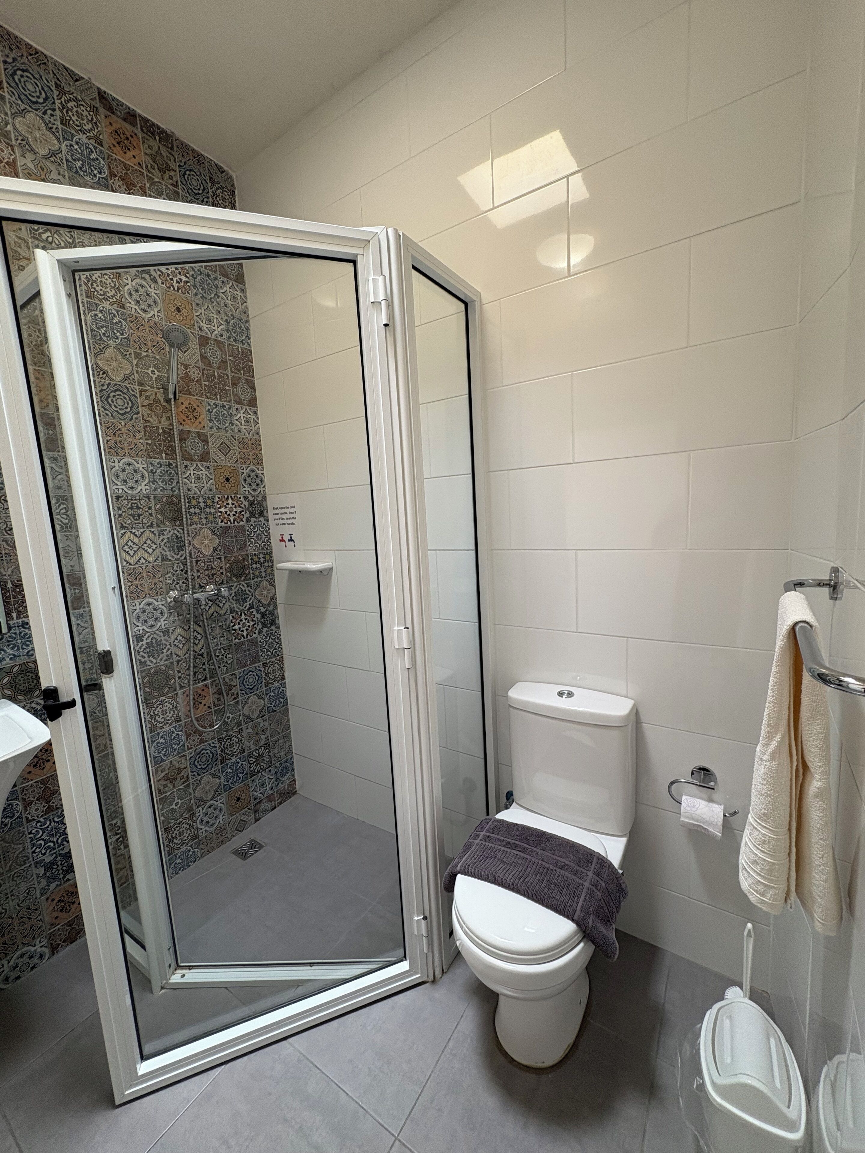 A bathroom with a shower enclosure, toilet, and a towel rack.