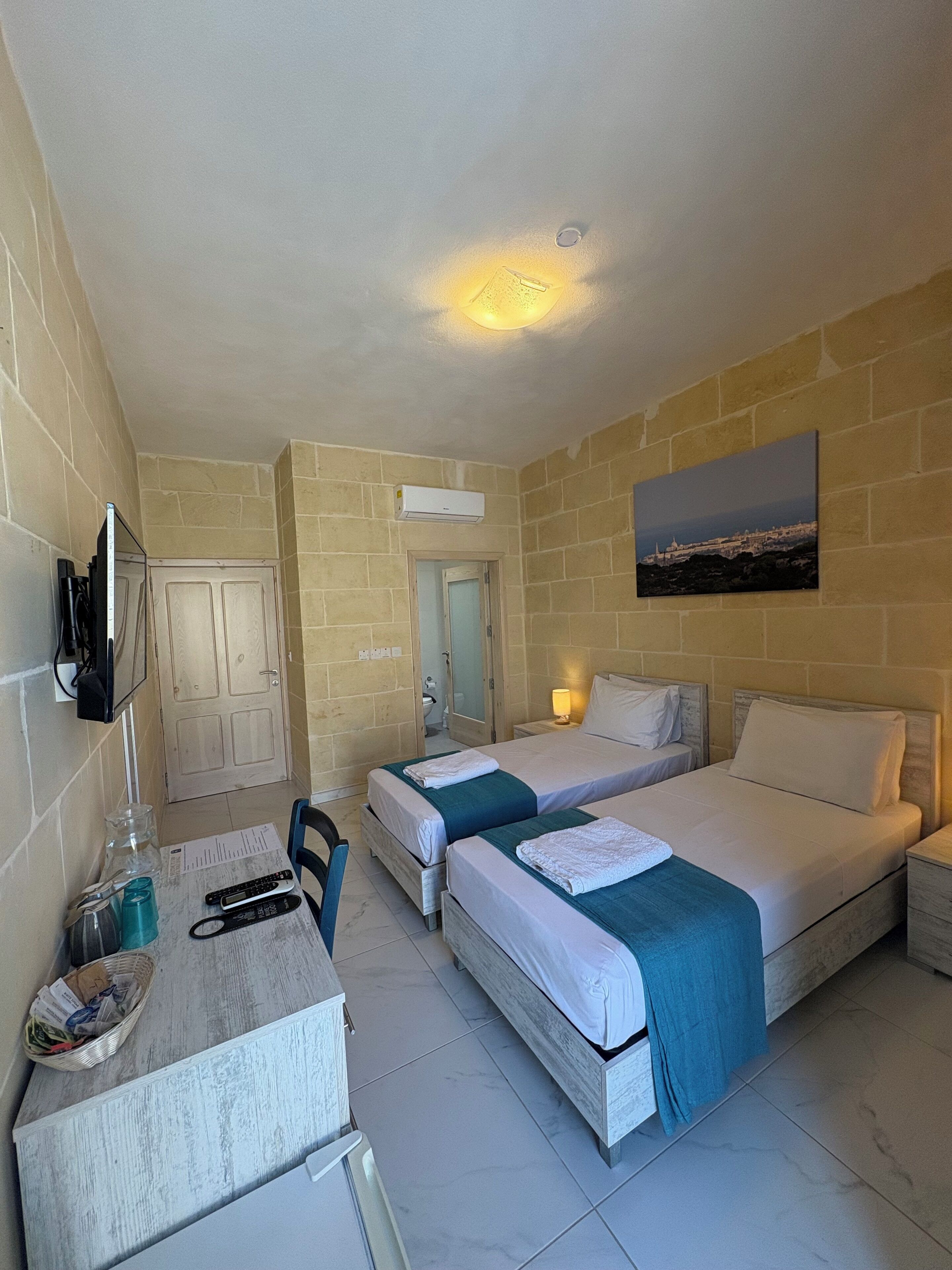 A hotel room with two beds, a desk, a television, and a painting on the wall.