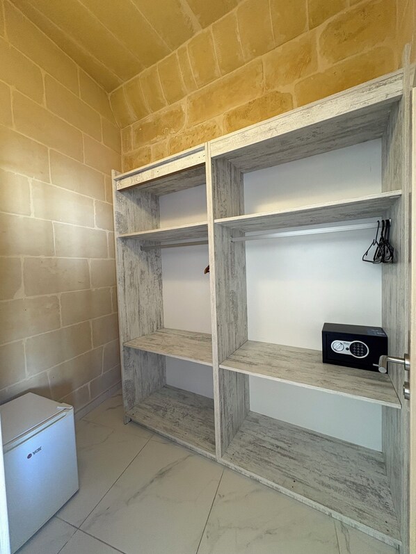 A room with a brick wall, a white refrigerator, and a wooden shelving unit with a black safe.