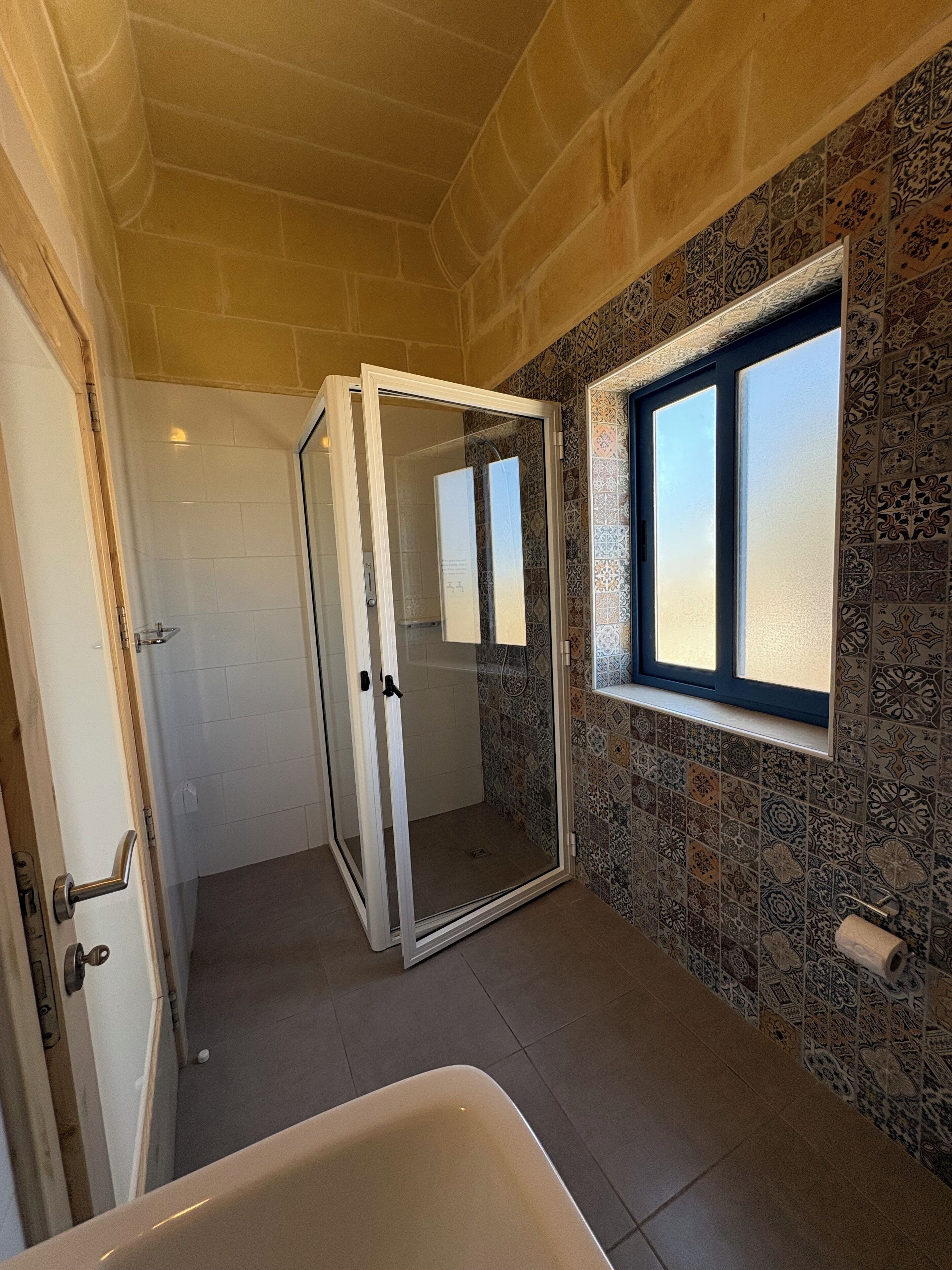 A bathroom with a shower, a window, and patterned tiles.