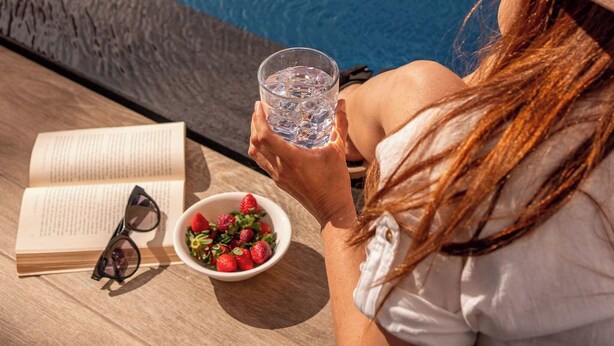 Una persona descansando junto a una piscina con un libro, gafas y un cuenco de fresas.