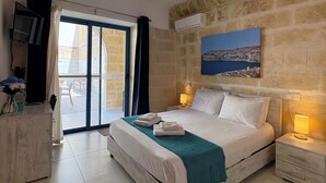 Una habitación de hotel con una cama grande, televisión, escritorio con silla y balcón con vista al mar.