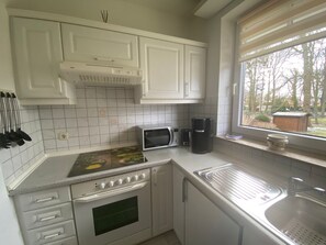 Eine Küche mit weißen Schränken, einer Mikrowelle, einer Kaffeemaschine und einem Fenster mit Blick auf Bäume und ein Haus.