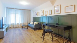 A modern living room with a sofa, a desk, and a chair. There are framed pictures on the wall and a television on a stand. - Schiffmeisterapartment Melk, Wachau - design meets history (Melk)